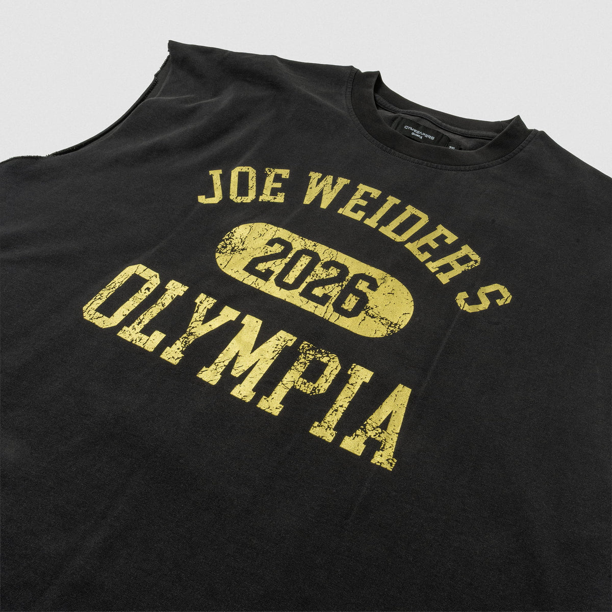 Close up view of front logo on the black Joes Olympia Cut-Off that says "Joe Weiders" in arching text, above
"2026" in a circle, and "OLYMPIA" wordmark text below