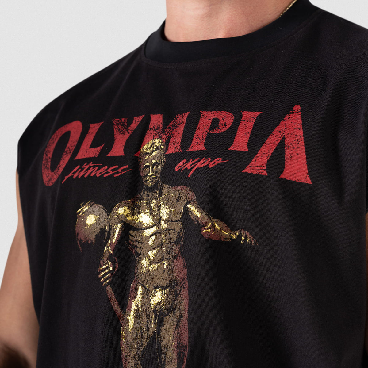 Close up view of the front graphic on the Olympia 2026 Sandow Cut-Off that says "OLYMPIA FITNESS EXPO" in distressed red text above the depiction of the gold Olympia statue