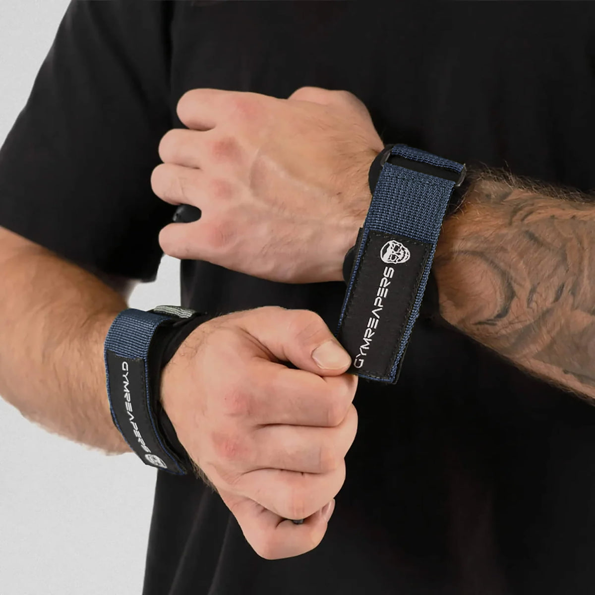 gymreapers athlete attaching navy lifting grips onto wrist, while the other one has it on already.
