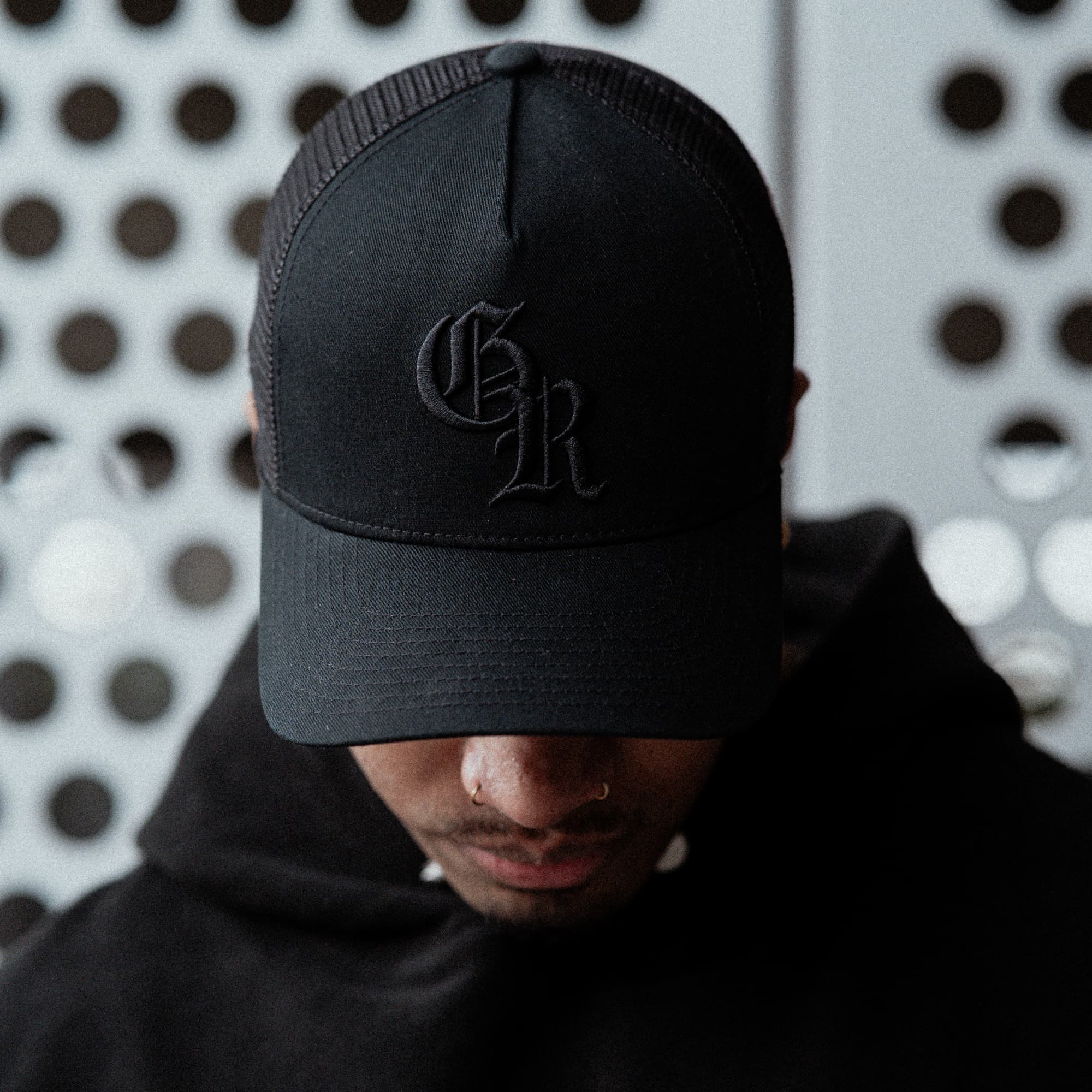 lifestyle shot of athlete wearing the Black/Black Initial Trucker Hat close up front view