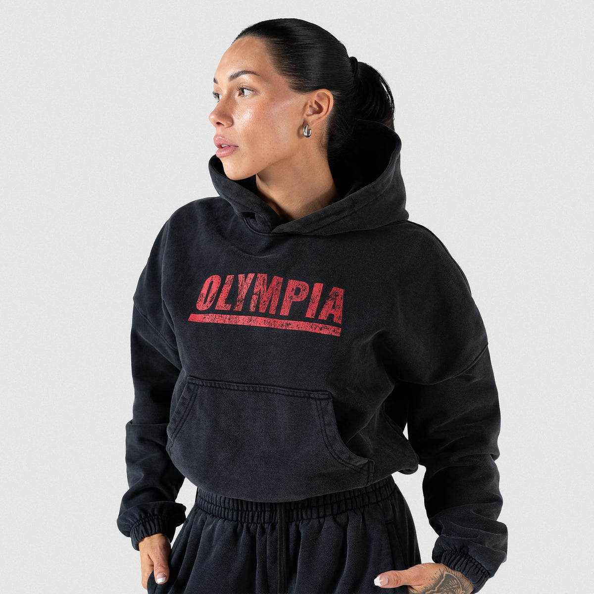 Championship Crop Hoodie | Front view, on model of black hoodie, featuring large Olympia front graphic and kangaroo pocket