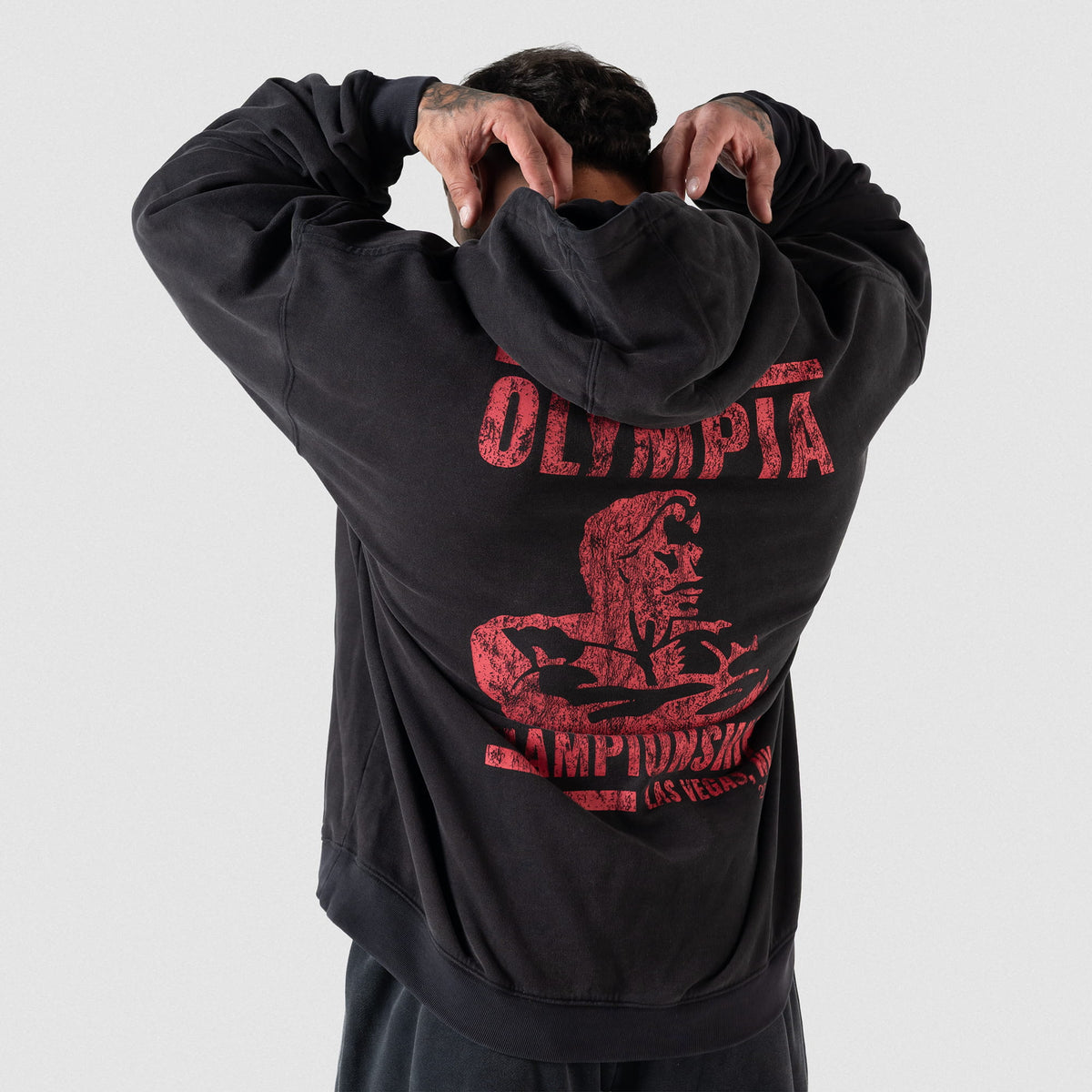 Championship Hoodie | Male model facing away to show the large red back logo of the Olympia Championship Las Vegas NV 2026 while pulling up his hood