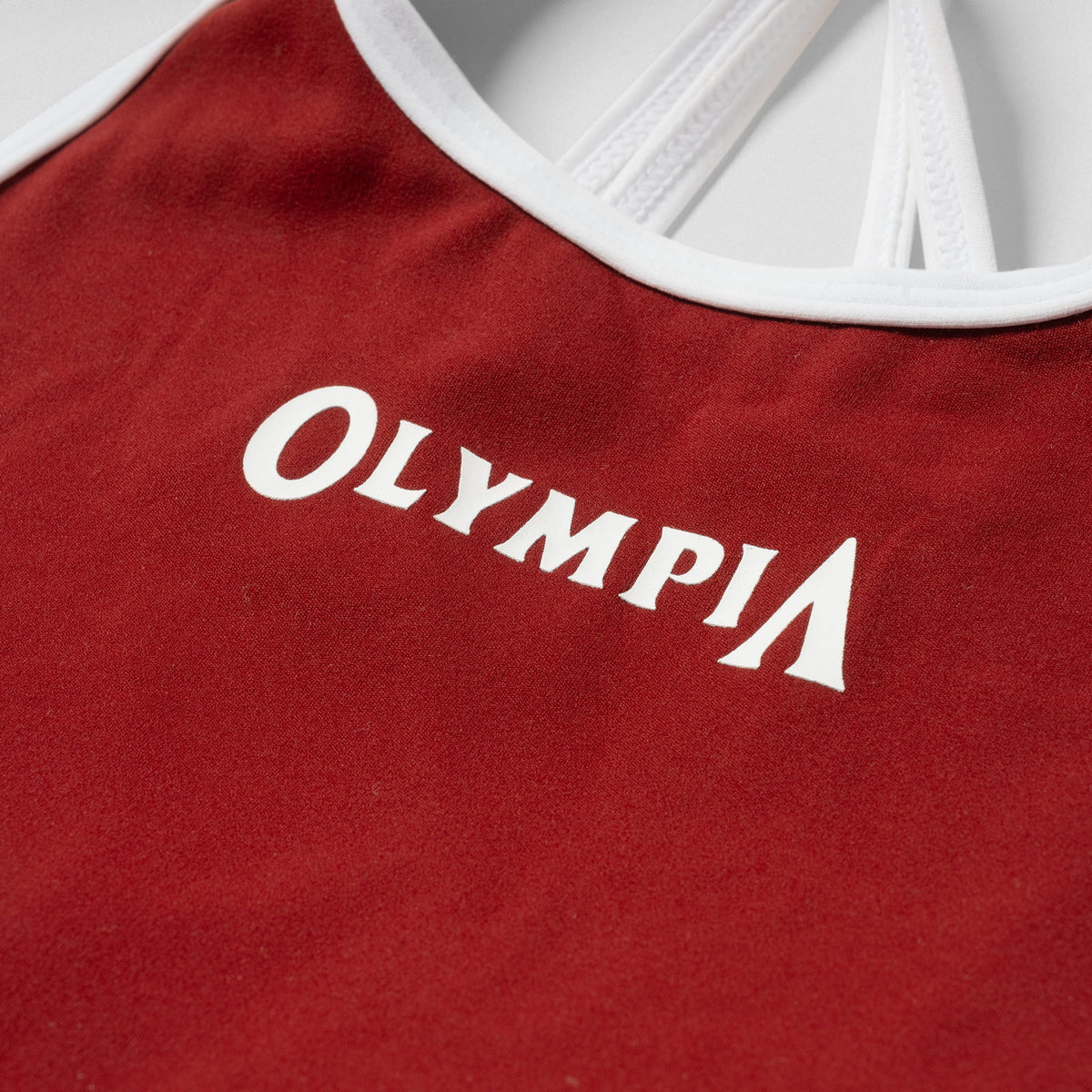 Close up view of the white "OLYMPIA" wordmark on the front chest of the Olympia High Neck Bra - Ember Red