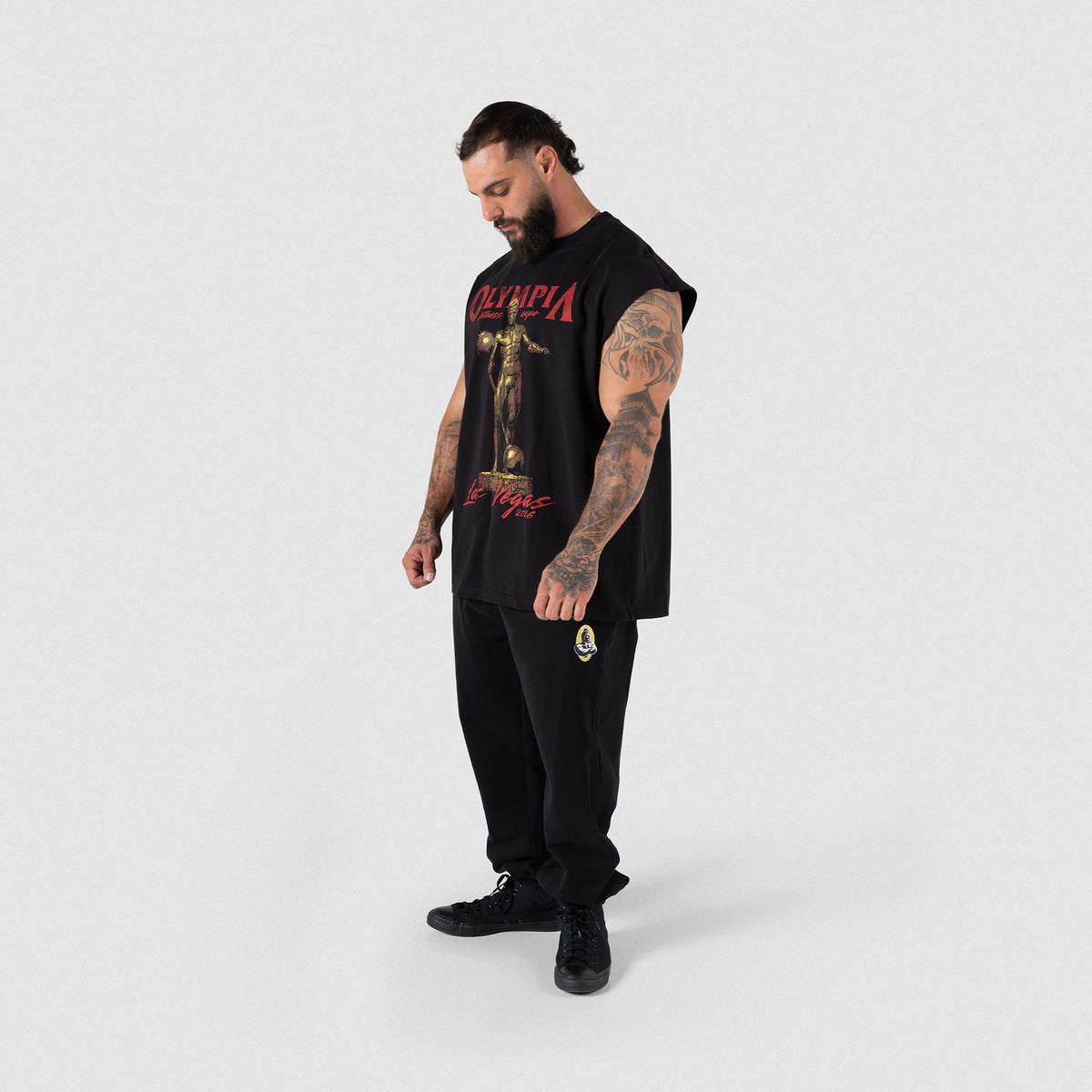 Side view of male model pairing the Olympia 2026 Sandow Cut-Off tank with black joggers