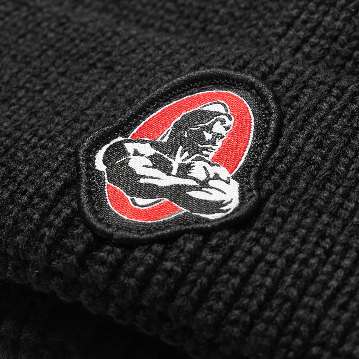 Close up of the classic Red, White, and Black Signature Olympia bodybuilding logo on the Signature Ribbed Knit Beanie