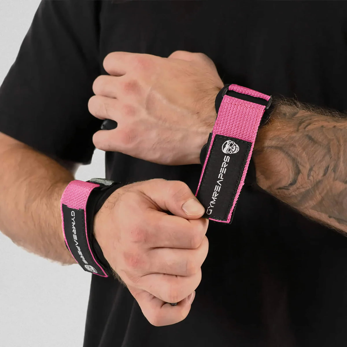 gymreapers athlete attaching pink lifting grips onto wrist, while the other one has it on already.