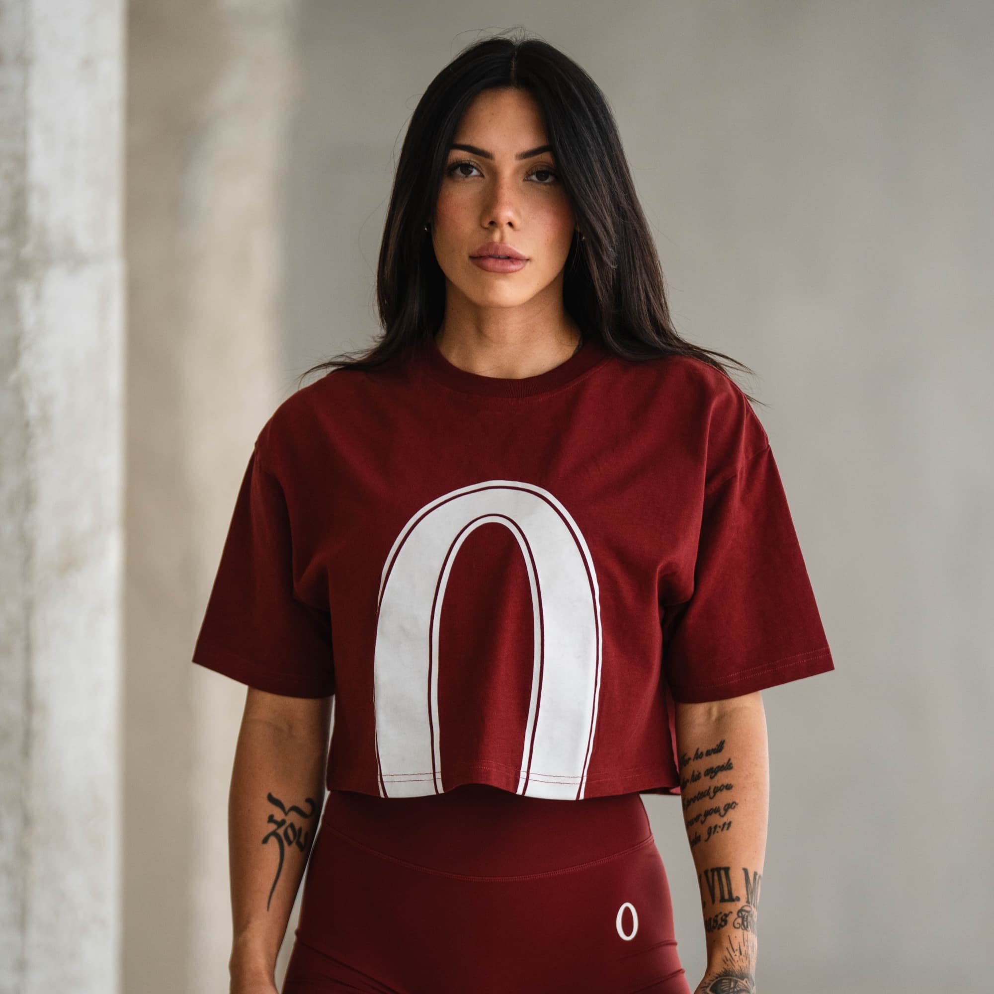 Female athlete wearing the Olympia Crop Tee in red with bold white “O” graphic, styled with matching shorts.