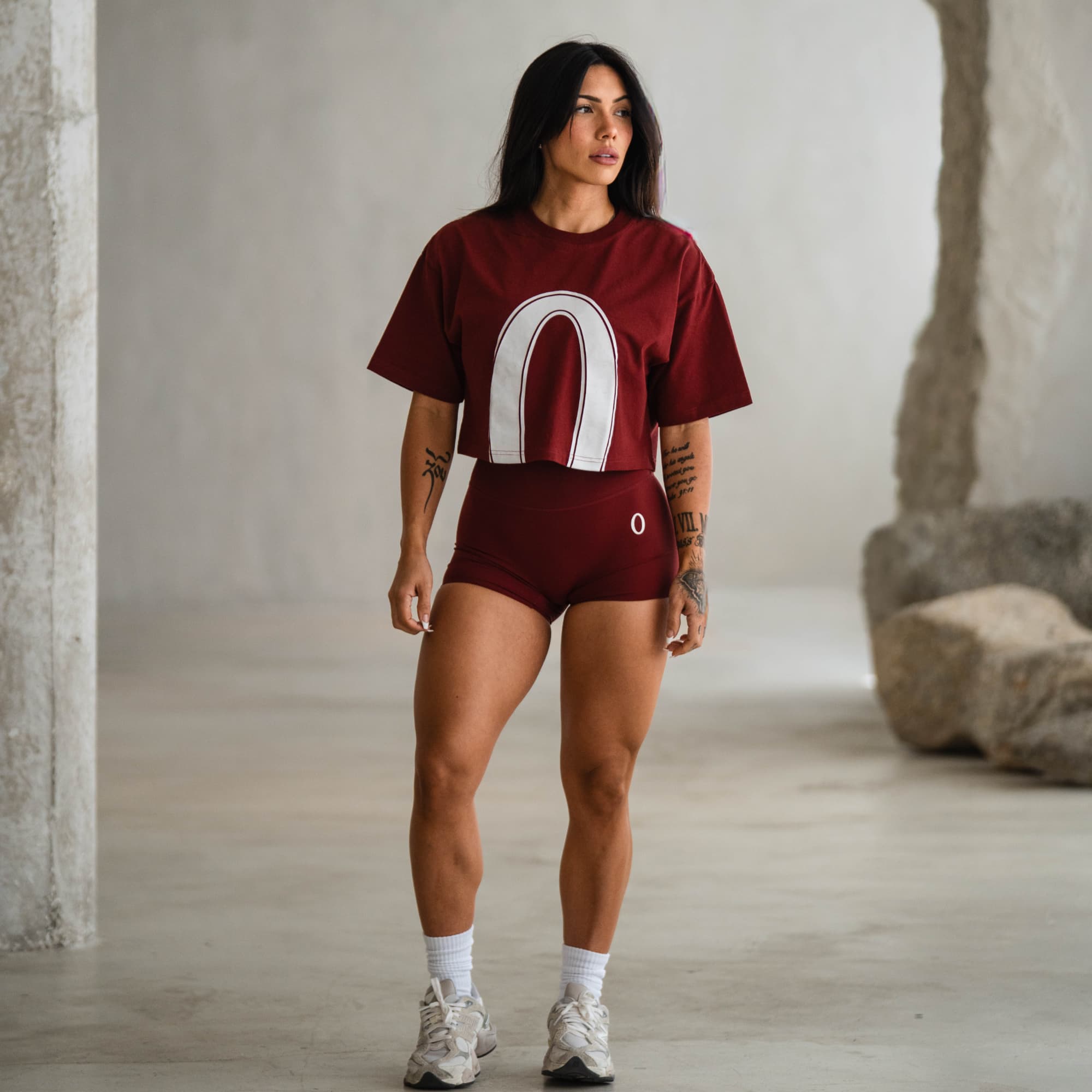 Female athlete modeling the Olympia Crop Tee and matching red shorts, styled in a minimal studio setting for the Olympia collection.