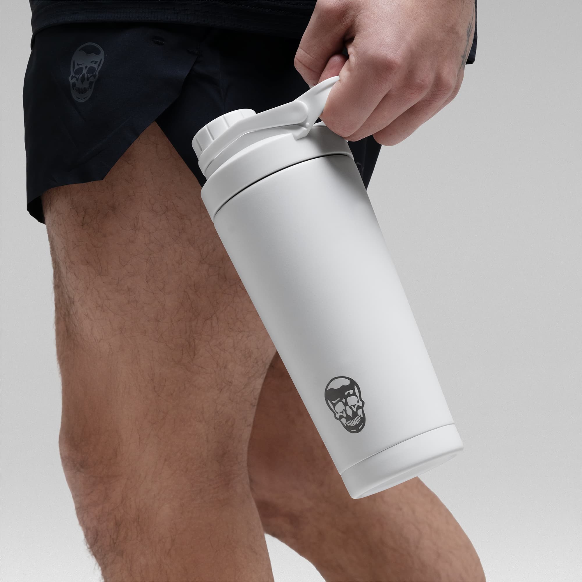 Athlete holding the White Stainless Steel Shaker by the built in carry loop showcasing skull logo