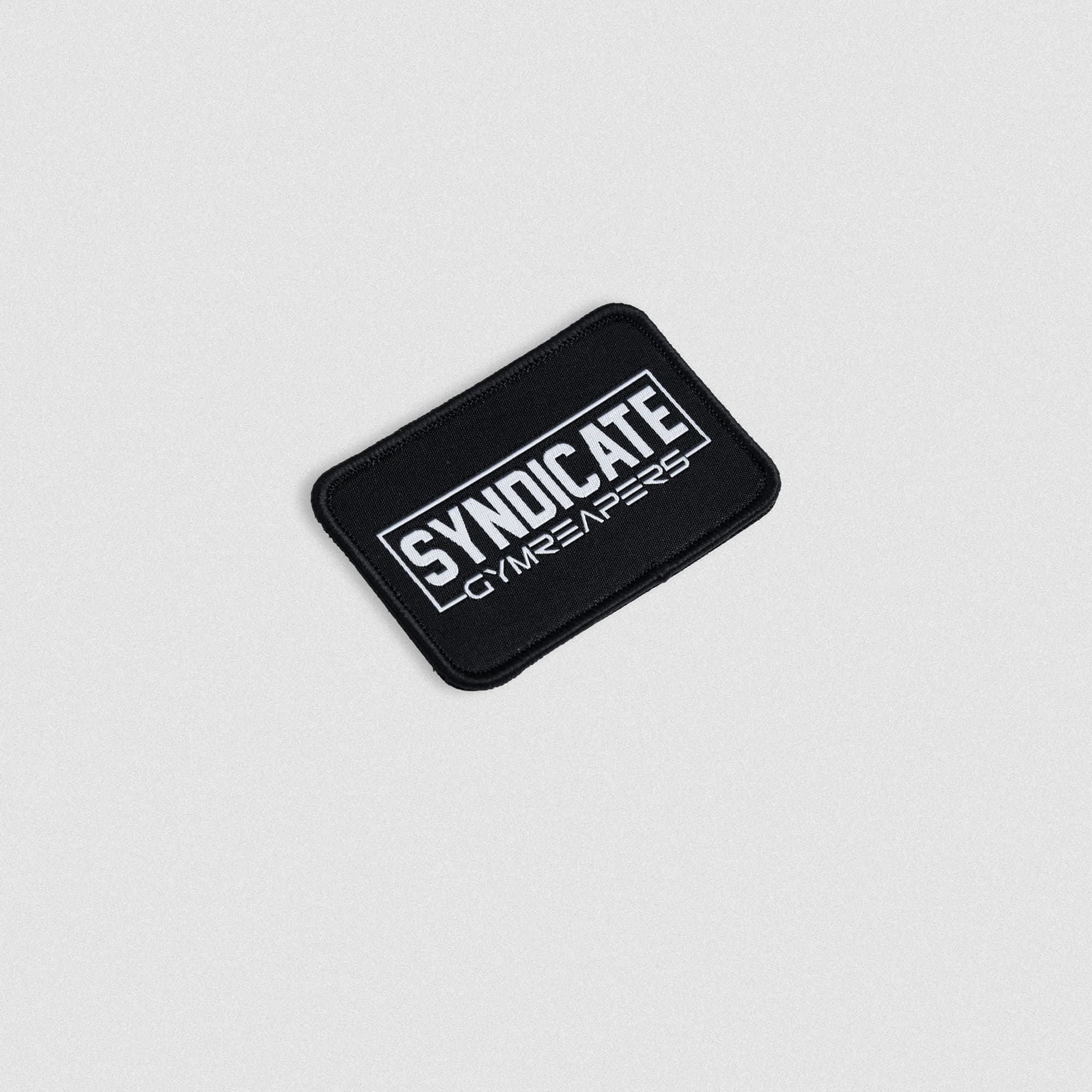 Angled view of the black SYNDICATE x GYMREAPERS patch with white embroidered text.